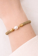 Gold bracelet with a pearl on a wrist against a white background