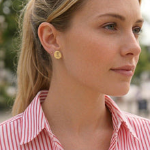 Woman wearing a gold earring with a visible brand logo.