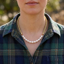 A close-up of a woman wearing a gold chain necklace with a strand of white freshwater pearls, styled with a green and blue plaid button-down shirt.