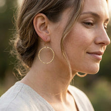 Woman wearing gold hoop earrings with a blurred natural background