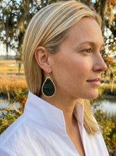 A blonde woman in a white collared shirt shown in profile outdoors, wearing a large teardrop-shaped dark green stone earring with a gold-tone border.