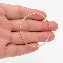 Hand holding a thin gold-tone hammered hoop for scale.