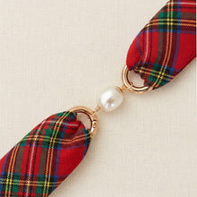 Red plaid ribbon with gold loops and a pearl on a beige background