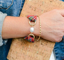 Close-up of a wrist wearing a colorful bracelet with pearl charm on a cork surface.