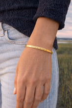 Gold bracelet on a wrist with a blurred natural background