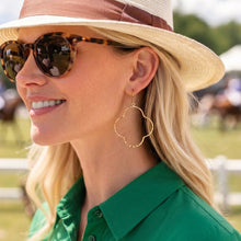 Woman wearing a straw hat, sunglasses, and gold earrings with a blurred outdoor background
