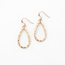 Rose gold teardrop earrings with white stones on a light beige background