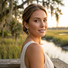 Woman standing by a body of water with trees and sunset in the background