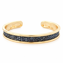 A gold cuff bracelet featuring a textured dark gray inlay channel, photographed on a clean white background.