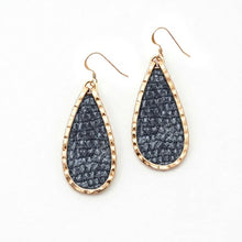 Teardrop-shaped earrings with gold frames and textured black stones on a white background