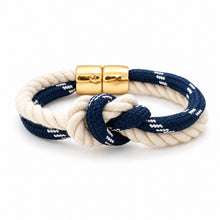 A rope bracelet with a knotted detail, featuring navy blue and cream white braided cords with gold magnetic clasp, on a white background.
