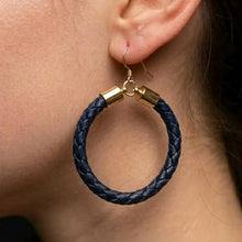 A close-up of a person's ear wearing a large braided hoop earring in dark navy blue with gold-tone metal caps and hooks.