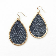 Teardrop-shaped earrings with textured dark gray stones and gold frames on a white background