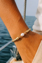 Gold bracelet with a pearl on a person's wrist by the sea