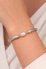 Silver bracelet with a pearl on a wrist against a neutral background