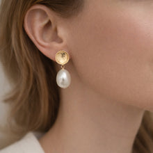 Gold earring with a pearl drop worn by a person