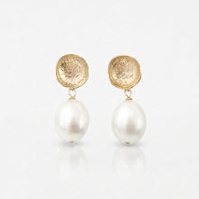 Pair of earrings with gold coin-like tops and white pearls on a light gray background