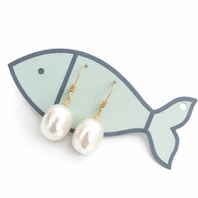 Pearl earrings on a fish-shaped earring stand with a white background