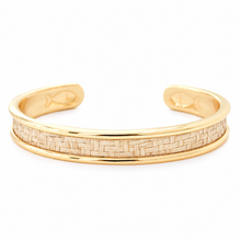 A polished gold cuff bracelet featuring a central woven natural fiber inlay, photographed on a clean white background.
