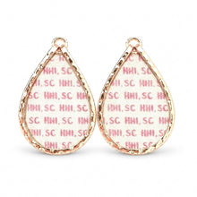A pair of teardrop-shaped earrings with textured rose gold metal borders and a white fabric insert printed with a pink repeating 'HMI, SC' pattern, shown on a plain white background.