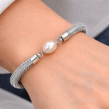 Silver bracelet with a pearl on a wrist against a neutral background