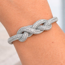 Silver knot bracelet on a wrist with a neutral background