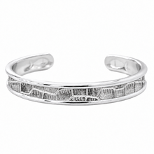 A polished silver-tone open cuff bracelet featuring a textured, geometric inlay pattern along the front, set against a plain white background.
