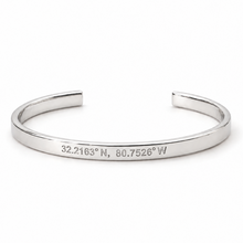 A polished silver open cuff bracelet engraved with the geographic coordinates '32.2163° N, 80. hilton head island