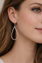 Close-up of a woman wearing silver hoop earrings with a neutral background