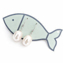 Pearl earrings on a fish-shaped earring stand against a white background