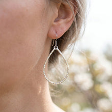 Silver hoop earrings worn by a person with a blurred natural background