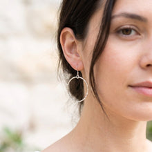 Close-up of a woman wearing silver hoop earrings with a blurred natural background