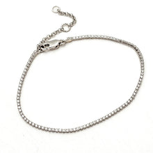 A silver tennis bracelet with a row of clear crystals, featuring a lobster clasp and an adjustable extension chain, displayed on a white background.