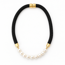 A black braided cord necklace with a curved section of white freshwater pearls, accented by gold-toned metal caps on a clean white background.
