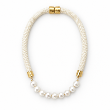 A statement necklace featuring a thick cream-colored braided cord, a curved section of white freshwater pearls, and polished gold-tone metal caps at the ends, shown on a plain white background.