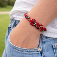 Person wearing a red and black braided bracelet on a blurred outdoor background