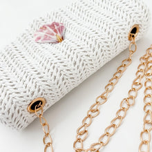 Gold chain necklace on a textured white surface with a pink shell.