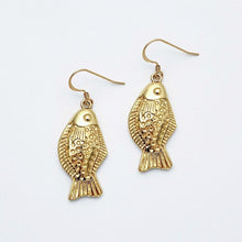 Gold fish-shaped earrings on a light gray background