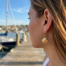 Close-up of a person wearing gold shell earrings with a marina background
