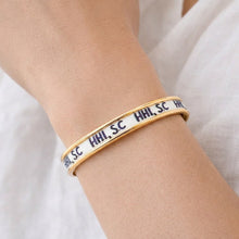 Gold bracelet with black text on a person's wrist against a white background