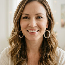 Woman with long brown hair wearing hoop earrings, smiling.