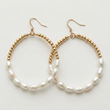 Pair of hoop earrings with gold beaded rims and white pearls on a light background