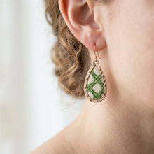 Teardrop-shaped earring with green pattern worn by a person on a white background