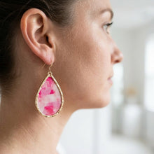 Close-up of a woman wearing a pink teardrop earring with a gold frame.