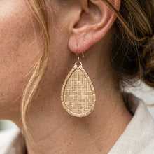 Close-up of a woman wearing a gold teardrop earring with a woven pattern.