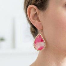 Teardrop-shaped pink earrings with gold accents worn by a person.