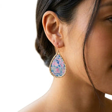 Close-up of a woman wearing a colorful teardrop earring with a gold frame.