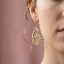 Close-up of a person wearing a gold teardrop earring against a pink background