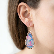 Close-up of a woman wearing a colorful teardrop earring with a blurred background