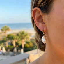 Close-up of a person wearing pearl earrings with a blurred beach and palm trees in the background